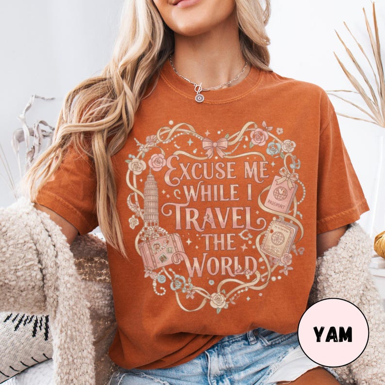 Vintage-inspired pink and beige travel-themed shirt with passport, suitcase, and the quote “Excuse Me While I Travel The World” framed in florals.