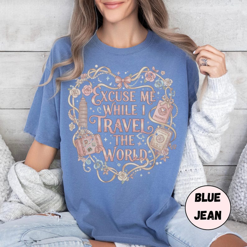 Vintage-inspired pink and beige travel-themed shirt with passport, suitcase, and the quote “Excuse Me While I Travel The World” framed in florals.