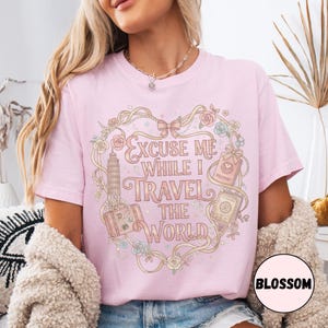Vintage-inspired pink and beige travel-themed shirt with passport, suitcase, and the quote “Excuse Me While I Travel The World” framed in florals.