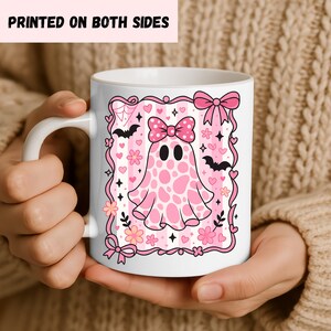 ceramic coffee mug featuring a pink spotted ghost with a bow, surrounded by bats, hearts, and flowers in a coquette aesthetic design