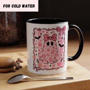 ceramic coffee mug featuring a pink spotted ghost with a bow, surrounded by bats, hearts, and flowers in a coquette aesthetic design