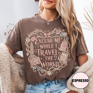 Vintage-inspired pink and beige travel-themed shirt with passport, suitcase, and the quote “Excuse Me While I Travel The World” framed in florals.