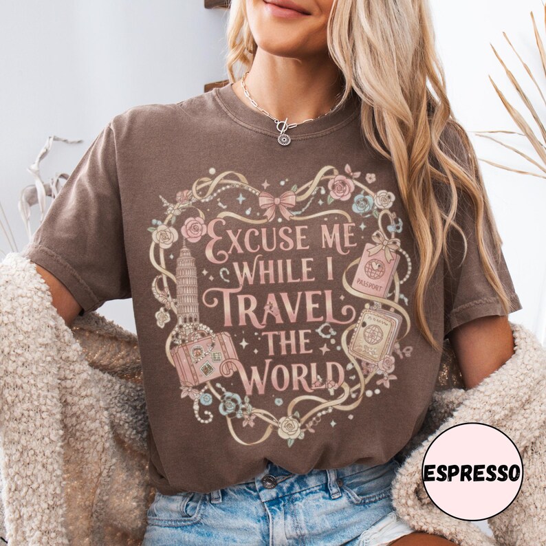 Vintage-inspired pink and beige travel-themed shirt with passport, suitcase, and the quote “Excuse Me While I Travel The World” framed in florals.