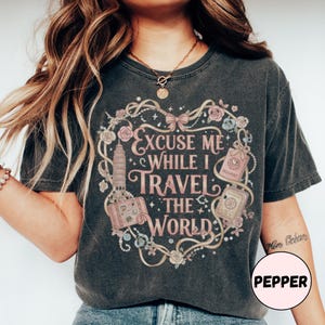 Vintage-inspired pink and beige travel-themed shirt with passport, suitcase, and the quote “Excuse Me While I Travel The World” framed in florals.