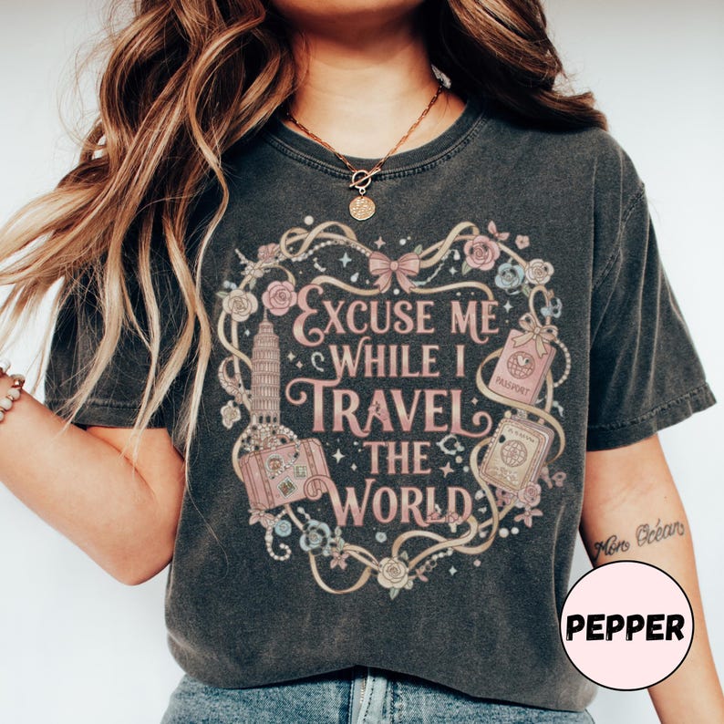 Vintage-inspired pink and beige travel-themed shirt with passport, suitcase, and the quote “Excuse Me While I Travel The World” framed in florals.