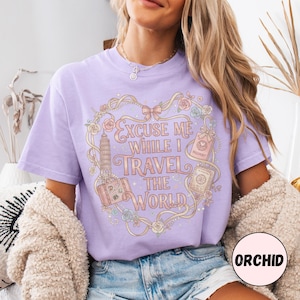 Vintage-inspired pink and beige travel-themed shirt with passport, suitcase, and the quote “Excuse Me While I Travel The World” framed in florals.