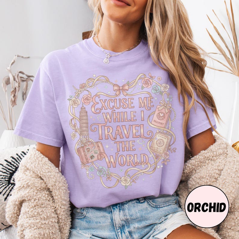 Vintage-inspired pink and beige travel-themed shirt with passport, suitcase, and the quote “Excuse Me While I Travel The World” framed in florals.