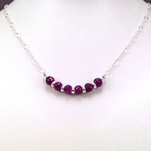 May include: A silver chain necklace with a row of purple gemstone beads.