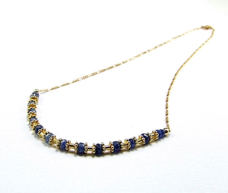 May include: A gold chain necklace with a row of dark blue gemstone beads.