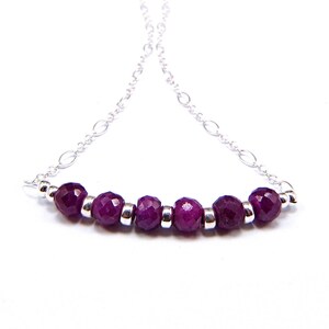 May include: A silver chain necklace with a row of seven faceted purple gemstones.