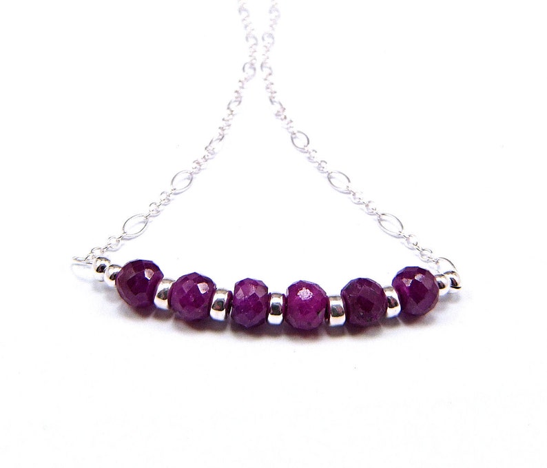 May include: A silver chain necklace with a row of seven faceted purple gemstones.