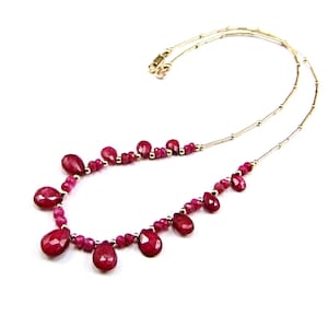 Könnte beinhalten: Eine goldene Kettenkette mit einem tropfenförmigen Rubin-Anhänger. Die Kette besteht aus kleinen goldenen Perlen und verfügt über mehrere Rubine.
