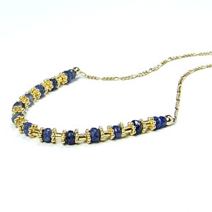 May include: A delicate gold chain necklace with a row of dark blue gemstone beads interspersed with gold beads.