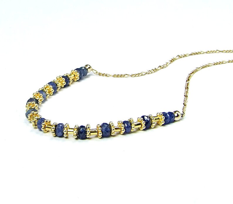 May include: A delicate gold chain necklace with a row of dark blue gemstone beads interspersed with gold beads.