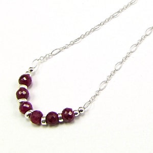 May include: A silver chain necklace with a row of small, faceted, dark red gemstones.
