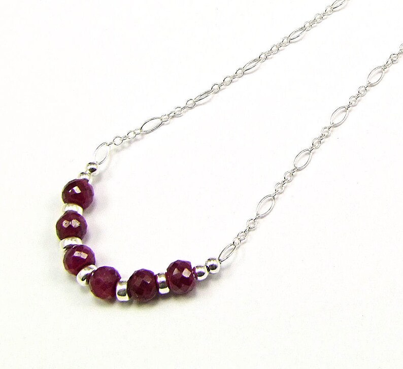 May include: A silver chain necklace with a row of small, faceted, dark red gemstones.