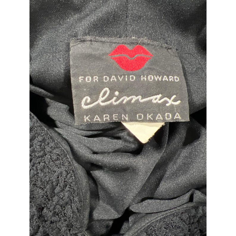 May include: Black dress with a black lace trim and a white tag. The tag says "climax for David Howard Karen Okada" with a red lip print.