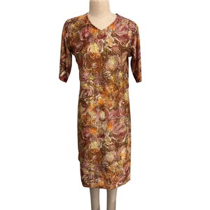 以下が含まれることがあります： Vネックと半袖の膝丈ワンピース。オレンジ、黄色、バーガンディの色合いの花柄が茶色の背景に描かれています。マネキンに着せられたワンピースです。