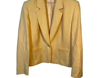 May include: A light yellow blazer with a notched lapel, two front pockets, and a single-button closure. The blazer is hanging on a wooden hanger. The garment is made of a soft, woven fabric.