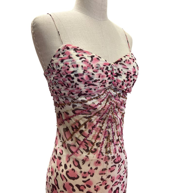 May include: A pink and black leopard print dress with spaghetti straps. The dress features a ruched bodice and is embellished with pink and gold beading. The dress is displayed on a mannequin.