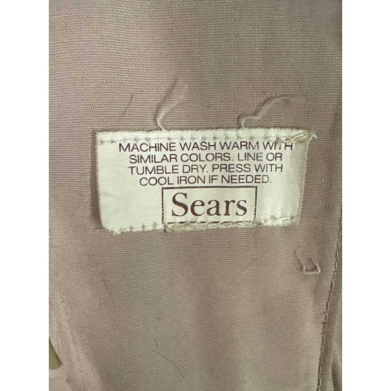 K&ouml;nnte beinhalten: Nahaufnahme eines beigefarbenen Stoffes mit einem eingen&auml;hten Etikett. Auf dem Etikett steht: "MACHINE WASH WARM WITH SIMILAR COLORS. LINE OR TUMBLE DRY. PRESS WITH COOL IRON IF NEEDED. Sears."
