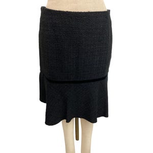 May include: A black tweed skirt with a flounce hem. The skirt has a straight silhouette with a velvet band detail at the waist. The skirt is displayed on a mannequin.