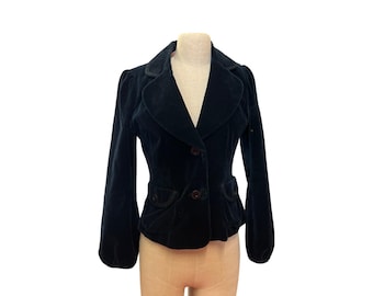 May include: A black velvet blazer with a classic design. The jacket features a notched collar, two-button closure, and two front pockets. The sleeves are long and slightly puffed at the shoulders. The blazer is displayed on a mannequin.