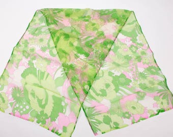 May include: A sheer scarf with a floral pattern in shades of green, pink, and white. The scarf is rectangular and appears to be made of a lightweight fabric. The floral design includes various flower shapes and sizes, creating a vibrant and colorful accessory.