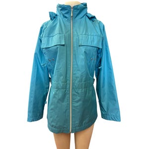 May include: A turquoise-blue jacket with a hood, two chest pockets, and a full-length zipper. The jacket has a cinched waist and long sleeves. The jacket is made of a lightweight material.