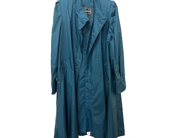May include: Teal-colored trench coat with a double-breasted design. The coat features a notched collar, shoulder epaulets, and a long, flowing silhouette. It is hanging on a black hanger against a white background.
