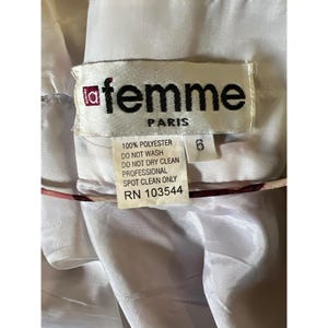 May include: A close-up of a clothing tag from "femme PARIS". The tag is white with black text, including "100% POLYESTER" and care instructions. The number "6" is printed on the tag. The background is a light-colored fabric.