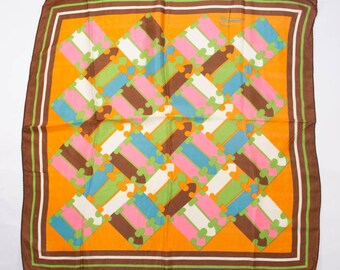 May include: A square scarf with a geometric pattern. The scarf features a vibrant orange background with a repeating design of interlocking shapes in pink, blue, green, brown, and white. The edges are bordered with brown, white, and green stripes.