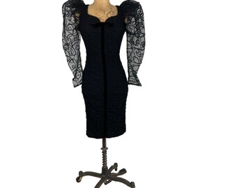 May include: A black dress with a sweetheart neckline and puff sleeves. The sleeves are made of sheer fabric with a floral pattern. The dress is fitted and has a midi length.