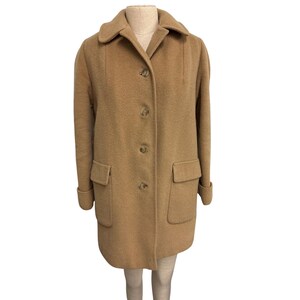 May include: A tan wool coat with a classic design. The coat features a collared neckline, button-down closure, two front pockets, and folded cuffs. The coat is displayed on a mannequin against a white background.