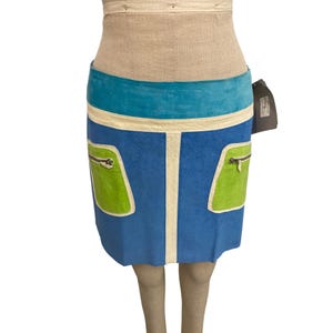Può includere: Gonna blu con fascia in vita turchese e due tasche verdi. La gonna presenta una striscia verticale bianca e bordi bianchi. Le tasche hanno cerniere argentate. Lunghezza di circa 40 cm.