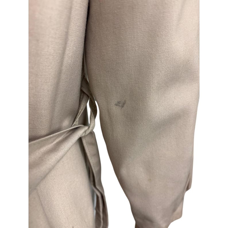 K&ouml;nnte beinhalten: Nahaufnahme eines beigefarbenen Kleidungsst&uuml;cks mit einem Bindedetail an der Taille. Der Stoff scheint glatt und leicht zu sein. Der &Auml;rmel ist sichtbar, und es gibt einen kleinen Fleck auf dem &Auml;rmel.