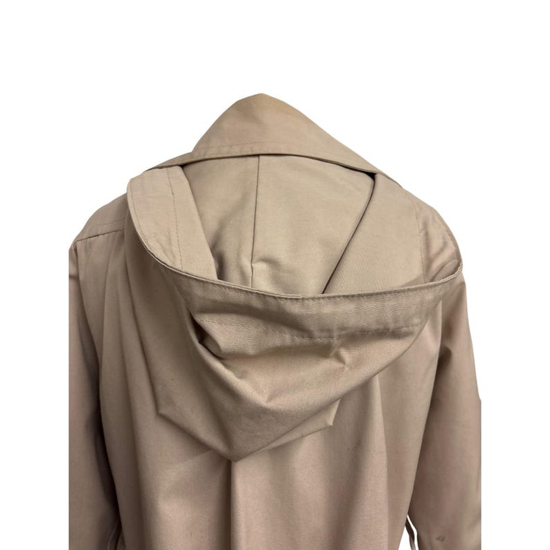 K&ouml;nnte beinhalten: Ein beigefarbener Mantel mit Kapuze, von hinten gesehen, mit hochgezogener Kapuze. Der Mantel ist einfarbig, und die Kapuze ist ein herausragendes Merkmal. Der Stoff scheint ein mittelschweres Material zu sein.