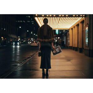 May include: A woman in a dark skirt and brown fur wrap stands on a city sidewalk at night. She holds a small black purse and a square print with the words "WEAR WHAT LOVE". The scene is lit by streetlights and a theater marquee.