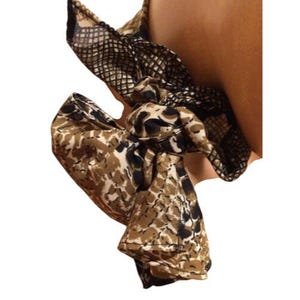 May include: A scrunchie with a brown, black, and tan animal print pattern. The scrunchie is made of a silky material and is tied in a bow. The scrunchie is a hair accessory.