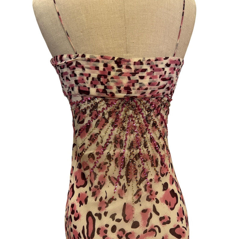 May include: A sleeveless dress with a pink and brown leopard print pattern. The bodice features a ruched design with a pink and brown pattern. The dress is embellished with pink and brown beads, and has thin spaghetti straps.