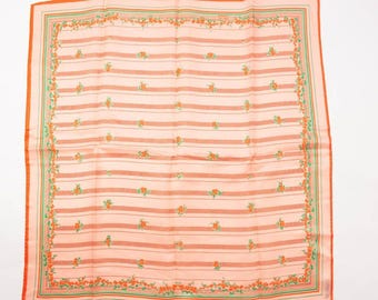 Op de afbeelding: Een vierkante, perzikroze sjaal met horizontale strepen en kleine bloempatronen. De sjaal heeft een oranje en groene rand, met een bloemenontwerp langs de randen. De sjaal is gemaakt van een lichtgewicht stof.