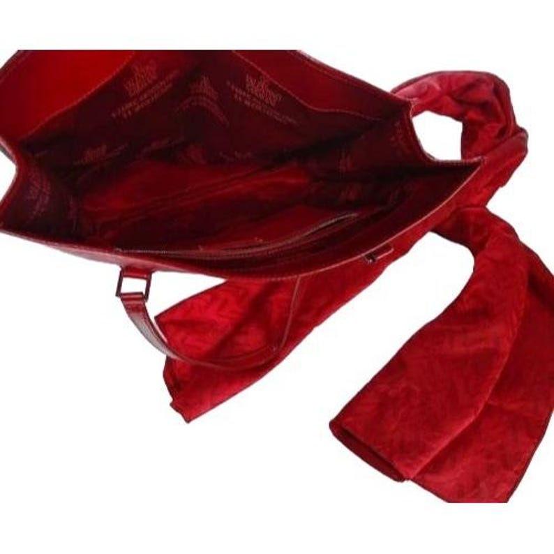 May include: A red leather tote bag with a matching scarf. The bag has a rectangular shape with a handle and a zipper closure. The scarf is draped over the bag. The interior of the bag is visible.