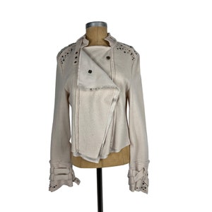 May include: Cream-colored jacket with an asymmetrical design. The jacket features a notched collar, long sleeves, and decorative metal studs along the shoulders and cuffs. The jacket is displayed on a mannequin.