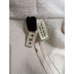 May include: Close-up of a cream-colored garment with a tag. The tag is black and reads "WE THE FREE" and "M". A smaller tag reads "MADE IN CHINA" and "FABRIQUE EN CHINE".