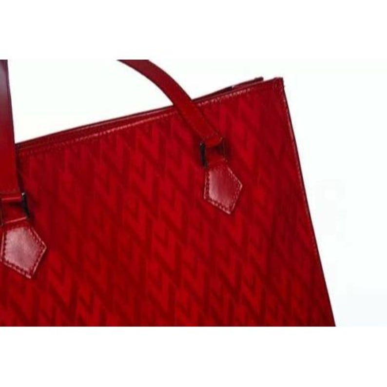 May include: A red tote bag with a geometric pattern. The bag has a glossy finish and features a top handle and decorative leather accents. The bag is designed with a structured shape.