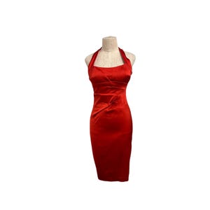 May include: A vibrant red satin halter dress displayed on a mannequin. The dress features a fitted bodice, a halter neckline, and a knee-length pencil skirt. The fabric has a subtle sheen, and the dress is designed to be form-fitting.