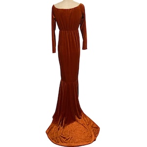 May include: A long, rust-coloured velvet dress with long sleeves and a mermaid-style skirt. The dress features a scoop neckline and a fitted bodice that flares out at the waist. The dress is floor-length.