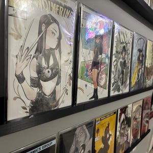 Puede incluir: Una colección de cómics exhibidos en estantes negros. El estante superior presenta varios cómics, incluido uno con un personaje de Wolverine. Los cómics están en fundas protectoras. La pared está pintada de gris.
