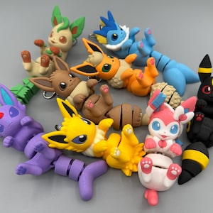 May include: A collection of colorful, stylized figurines of various Pokémon characters. The figures are in a variety of poses and colors, including green, blue, yellow, pink, and black. Each figure has a keychain attachment.
