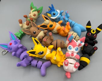 May include: A collection of colorful, stylized figurines of various Pokémon characters. The figures are in a variety of poses and colors, including green, blue, yellow, pink, and black. Each figure has a keychain attachment.
